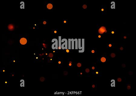 Orange Bokeh auf schwarzem Hintergrund, brennende und verschwommene Funken aus dem Feuer. Partikel brennender Glut fliegen und glühen isoliert am Nachthimmel 2021. Stockfoto