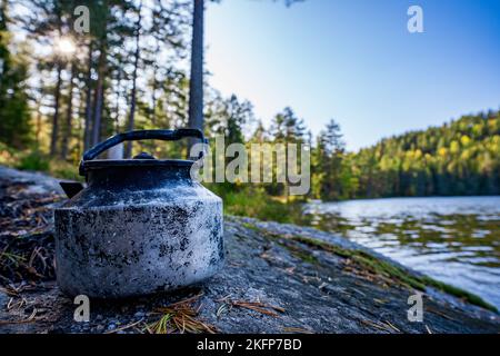 Ein alter klassischer Teekessel aus Metall, der auf dem Boden an einem Fluss im Wald aufgestellt wurde Stockfoto
