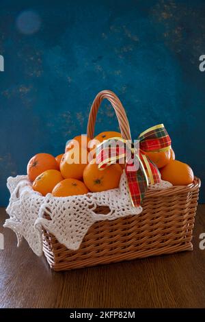 Mandarinen liegen in einem Korb auf blauem Hintergrund. Auf dem Korb befindet sich eine rote Schleife. Stockfoto