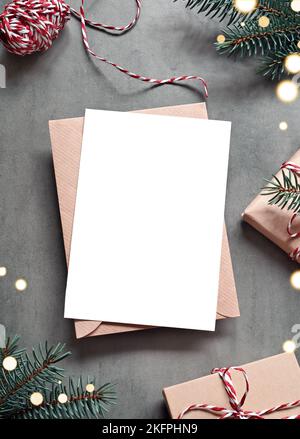 Leere weiße Papierkarte mit braunem Umschlag, Weihnachtskiefer und handgefertigter Geschenkbox auf grauem Hintergrund. Weihnachtskonzept. Stockfoto