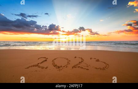 Schöner Sonnenuntergang mit 2023! Frohes neues Jahr 2023 Konzept! Jahr 2023 geschrieben im Sand am Strand mit dem Meer im Hintergrund Stockfoto