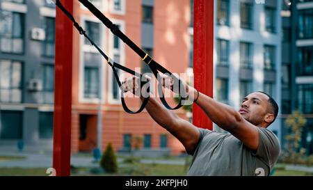 Muskulös athletisch kraftvoll Latino amerikanischer Mann Bodybuilder Sportler verwenden Sportgeräte Outdoor Stretching Workout auf Stadt Sport Boden hängenden Zug Stockfoto