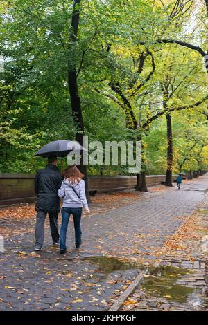 Ein Paar, das an einem regnerischen Nachmittag in New York City, NY, die Fifth Avenue in der Nähe des Central Park entlang läuft. Stockfoto