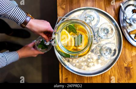Frau gießt Limonade in Glas. Nahaufnahme Teilansicht von oben, in der junge Frau Glas hält und gesunde Limonade aus dem Glas gießt. Erfrischende Bevera Stockfoto