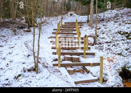 Unbearbeitete Holztreppe im Wald. Wiederherstellung des Naturparkweges. Naturpark Skanaiskalns. November ist der erste Schnee in Mazsalaca in Latv Stockfoto
