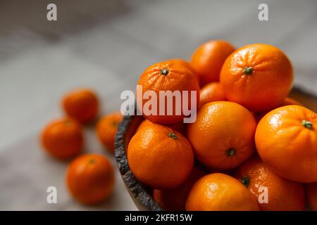 Korb mit Mandarine oder orangen Früchten auf grauem karierten Hintergrund. Bio-Lebensmittel. Stockfoto
