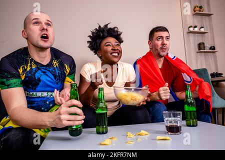 Freunde schauen sich ein Fußballspiel im Fernsehen an, trinken Bier und essen Chips, jubeln ihre Nationalmannschaft an. Stockfoto