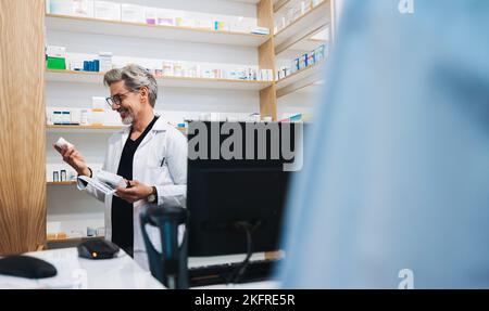 Ein reifer Apotheker liest das Medikamentenetikett, während er einem Patienten in einer Drogerie hilft. Medizinisches Fachpersonal, das ein ärztliches Rezept in einem ausgibt Stockfoto