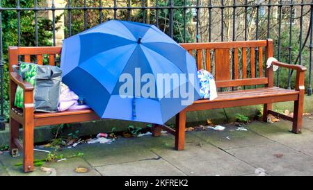 Obdachlose, die auf einer Bank im Regen unter einem Schirm in der Princes Street Edinburgh, Schottland, Großbritannien, schlafen Stockfoto