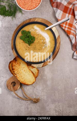 Rote Linsen Suppenpüree in dunkler Schüssel mit Brot auf grauem Marmortisch Stockfoto
