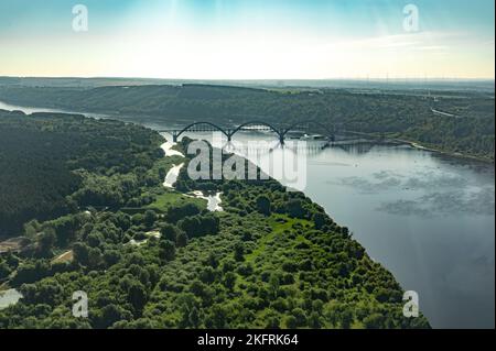 Luftaufnahmen aus einem Flugzeugfenster. Flugflug über den Fluss mit Brücke bei Sonnenaufgang. Flug über Straße und Fluss in der Nähe der Eisenbrücke Stockfoto