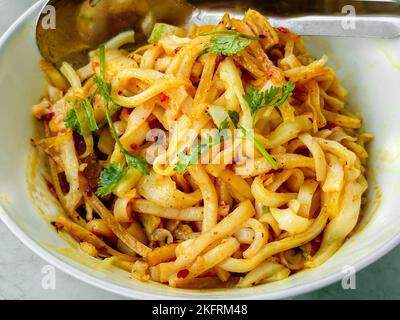 Myanmar traditioneller oder klassischer weißer flacher Nudelsalat namens Khauk SWE Thoke in weißer Schale. Nahaufnahme. Stockfoto