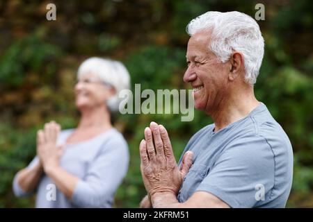 Yoga- gut für Körper, Geist und Seele. Ein älterer Mann, der mit seiner Frau im Freien Yoga macht. Stockfoto