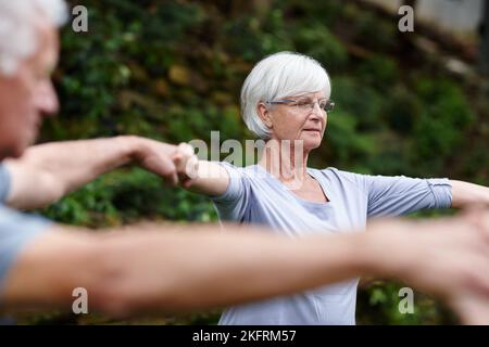 Achtsamkeit üben. Eine ältere Frau hält die Hände mit den Menschen, die mit Yoga machen. Stockfoto