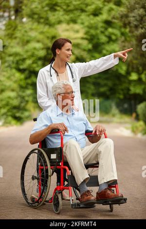 Genießen Sie die Schönheit der Natur auf Rädern. Eine Ärztin, die ihre ältere Patientin zu einem Ausflug in seinen Rollstuhl mitnimmt. Stockfoto