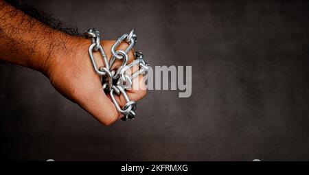 Eine Metallkette ist um eine Faust auf einem dunklen, verwischten Zement-Hintergrund mit Kopierraum gewickelt Stockfoto