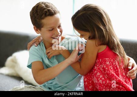 Ein Bruder und eine Schwester kitzeln sich gegenseitig auf dem Sofa. Stockfoto