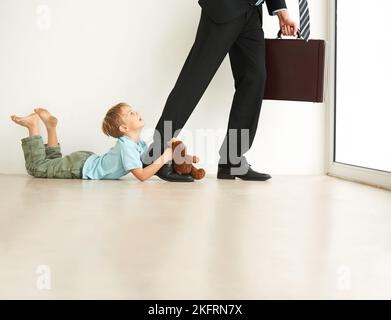 Nein, gehen Sie nicht hin. Ein kleiner Junge auf dem Boden, sehr unglücklich, dass sein Faher zur Arbeit geht. Stockfoto