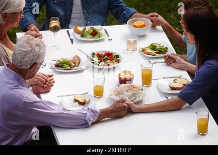 Dankbar für das, was sie essen werden. Eine Familie mit mehreren Generationen, die vor dem gemeinsamen Essen Gnade sagt. Stockfoto