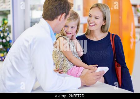 Wo tut es weh. Ein Apotheker, der einer Mutter und Tochter Medikamente gibt. Stockfoto