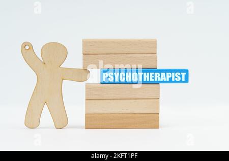 Medizin- und Gesundheitskonzept. Eine menschliche Figur schiebt einen blauen Holzblock beschriftet - PSYCHOTHERAPEUT aus einer Wand von Blöcken. Stockfoto