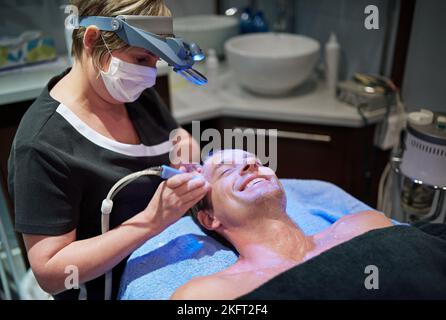 Moderne Schönheitsbehandlungen für einen jünger aussehenden Menschen. Ein Mann, der in einer Schönheitsklinik eine nicht-invasive Gesichtslift bekommt. Stockfoto