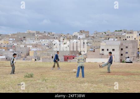 Jungen spielen Fußball, hinter ihnen Häuser und Wohnungen der ärmeren Bevölkerung, Siedlung außerhalb Fes, Marokko, Afrika Stockfoto