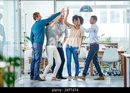 Nun, machen Sie es gemeinsam. Eine positive Gruppe von Mitarbeitern, die sich gegenseitig hoch-fiving, während sie im Büro stehen. Stockfoto