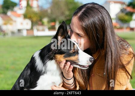 Junge Frau in legerer Kleidung küssen liebenswert Grenze Collie schaut weg an sonnigen Tag Stockfoto