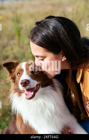 Junge Frau in legeren Kleidern küssen liebenswert Border Collie an sonnigen Tag Stockfoto