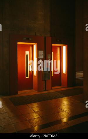 Inneneinrichtung eines leeren Flurs mit Fliesenboden im dunklen Raum und geöffneten Aufzugstüren mit Lampen Stockfoto