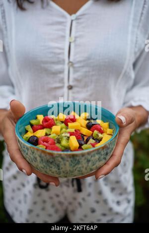 Von oben weicher Fokus der anonymen Frau demonstriert Schüssel mit gesunden Obstsalat am Sommertag im Hof Stockfoto