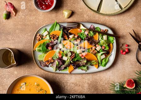 Draufsicht auf Kürbissalat mit Salat und Spinat, garniert mit Walnüssen und Granatapfelkernen und serviert auf dem Teller neben Suppe und Beerensauce Stockfoto