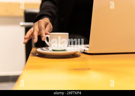 Crop anonyme Freiberuflerin sitzt im Café mit einer Tasse heißes Getränk, während an Netbook aus der Ferne arbeiten Stockfoto