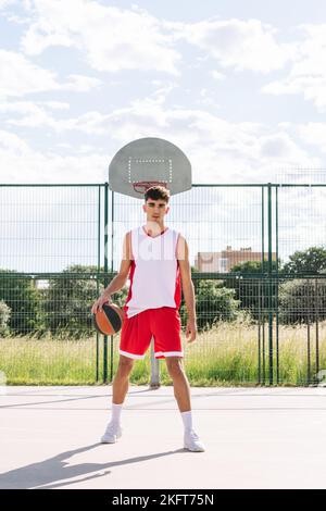 Entschlossener kaukasischer männlicher Streetball-Spieler, der im Sommer auf dem Sportplatz steht Stockfoto