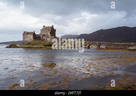 Altes Schloss auf Eilean Donan Insel in der Nähe von Brücke gegen bewölkten grauen Himmel in See in Schottland Stockfoto