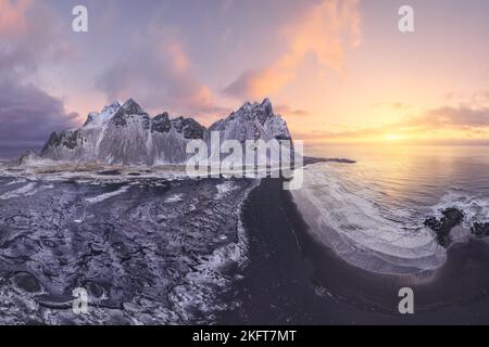 Ruhiges, gefrorenes, endloses Meer, umgeben von schwarzem, gefrorenem Sand und hohem, schneebedeckten Berg Vestrahorn bei einem malerischen Sonnenuntergang am Stockness Beach, Icel Stockfoto