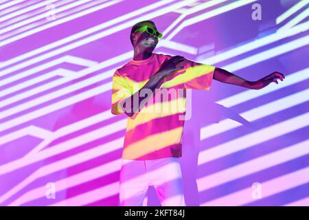 Ein ganzer Körper von fröhlichen afroamerikanischen Männern in trendigen Freizeitkleidung und Brillen, die im beleuchteten Studio tanzen Stockfoto