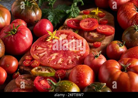 Hoher Winkel von geschnittenen Tomaten zwischen reifen ganzen roten Tomaten mit Wassertropfen Stockfoto