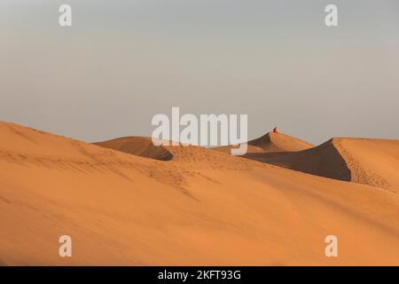 Anonyme Person, die an einem sonnigen Tag auf abgelegenen Dünen sitzt Stockfoto