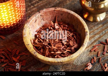 Rote Sandelholz-Chips in einer Schüssel, mit einer Duftlampe im Hintergrund. Zutat für ätherische Öle. Stockfoto