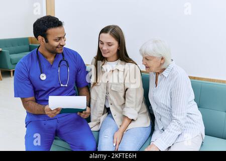 Doktor, der älteren Frau Patient gute Nachrichten über ihre Gesundheit nach der Behandlung im Krankenhaus erzählt, während er auf der Couch im Flur der medizinischen Einrichtung mit sitzt Stockfoto