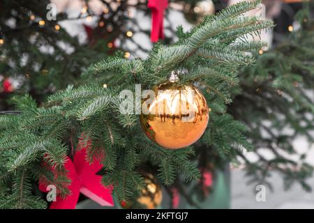 Goldene Weihnachtskugel und rote Ornamente, die während des Advents an einem Zweig des Weihnachtsbaums auf einem Jahrmarkt hängen Stockfoto