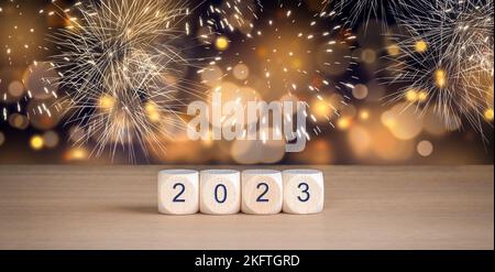 2023 - Holzwürfel mit Jahreszahl. Silvesterfeier mit Feuerwerk und abstrakten, verschwommenen Lichtern im Hintergrund. Stockfoto