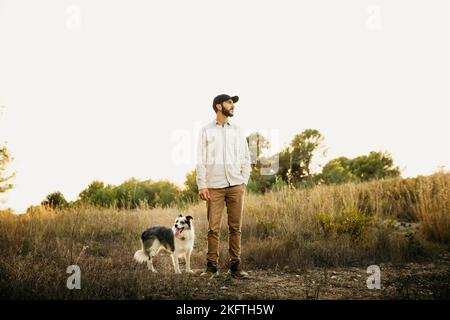 Porträt eines jungen bärtigen Mannes mit schwarzer Mütze und seinem Hund auf dem Land Stockfoto