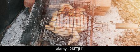 Huhn Fleisch Essen gebraten Grill auf schwelende Kohlen oder Ember vom Lagerfeuer auf dem Boden am Sommer oder Herbsttag. Grill in Camping-Bedingungen. Überleben o Stockfoto