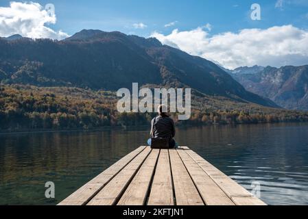 Sitzen auf einem kleinen Steg und genießen den Blick auf die Landschaft des Bohinjer Sees im Triglav Nationalpark, den Julischen Alpen, Slowenien Stockfoto