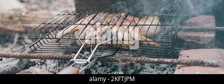 Hühnerfleischfutter werden auf dem Grill auf schwelenden Kohlen oder vom Lagerfeuer am Boden am Sommer- oder Herbsttag gebraten. Grill in Campingbedingungen. Sur Stockfoto