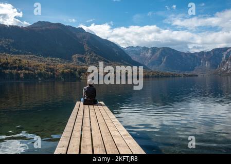 Sitzen auf einem kleinen Steg und genießen den Blick auf die Landschaft des Bohinjer Sees im Triglav Nationalpark, den Julischen Alpen, Slowenien Stockfoto