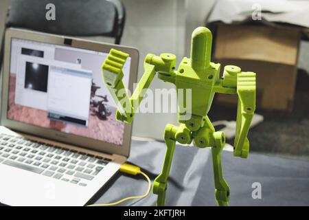 Ein 3D-gedruckter Roboter mit beweglichen Gliedmaßen, der neben einem Laptop steht Stockfoto